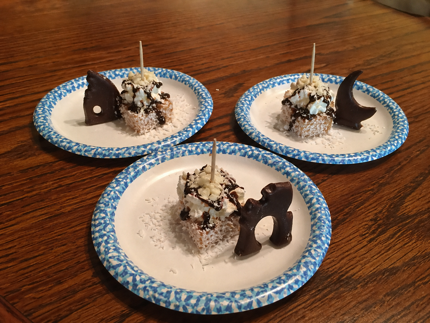 Three small plates with chocolate-coated coconut-covered cake pieces decorated with chocolate fish-shaped pieces and white toppings